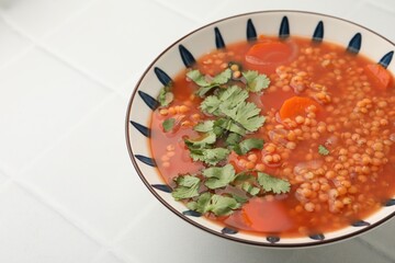 Tasty lentil soup in bowl on white tiled table, closeup. Space for text