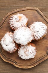 Tasty profiteroles with powdered sugar on wooden table, top view