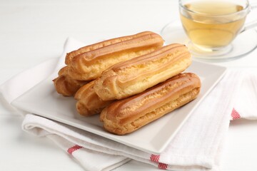 Tasty eclairs and tea on white wooden table, closeup