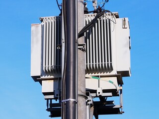 Distribution transformer mounted on a power line pole, close-up, against a blue sky background