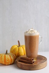 Delicious pumpkin latte with whipped cream, cinnamon sticks and fresh vegetables on white table near grey wall, closeup. Space for text