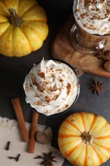 Delicious pumpkin latte with whipped cream, spices and fresh vegetables on dark textured table, flat lay