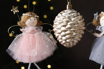 Obraz premium Beautiful Christmas decor and fairy dolls hanging against black background with blurred lights, closeup