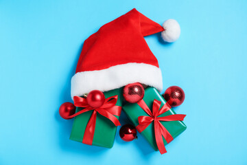 Santa hat with gift boxes and baubles on light blue background, flat lay. Merry Christmas and Happy New Year