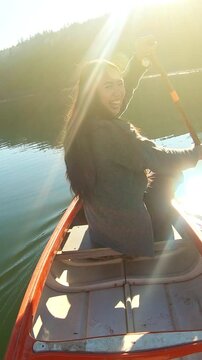A woman paddles a canoe on a serene lake at sunset, capturing tranquility and connection with nature. The warm sun enhances the peaceful setting, ideal for weekend activities and an active lifestyle.