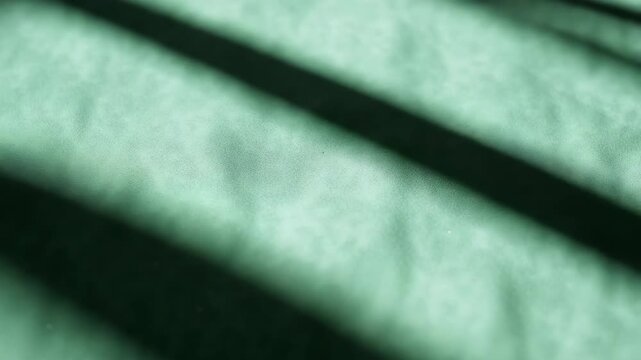 Close-up of textured green fabric with shifting shadows creating patterns showcasing a subtle play of light and texture from different angles throughout the video.