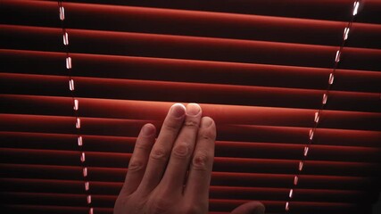 Man moves his left hand down, touching the closed red blinds - Powered by Adobe