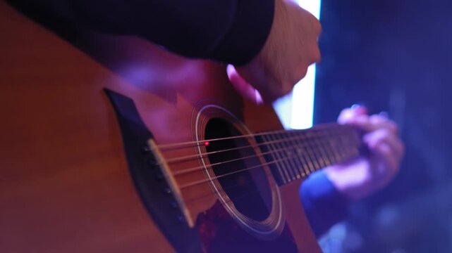 Male musician plays an acoustic guitar on stage under backstage spotlights