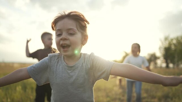 Children run and play together in sunlit grass field with arms outstretched smiling faces child laughter implied happy outdoor energy sunlight flare and movement children explore nature and run freely