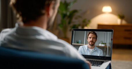 Man participating in a serious video call on laptop in cozy home environment with blurred background and warm lighting