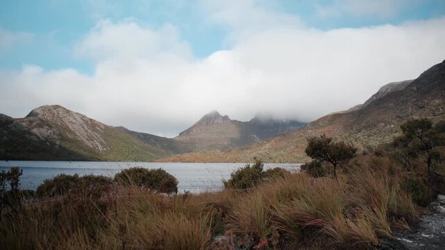 Scenic view of Cradle Mountain and Dove Lake, Tasmania. Clouds shroud the jagged peaks above the alpine lake and native grassy wilderness foreground.