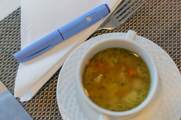 diabetes medication injection pen Ozempic soup meal restaurant table setting blue device white napkin fork close up gray placemat concept of healthcare nutrition and diet