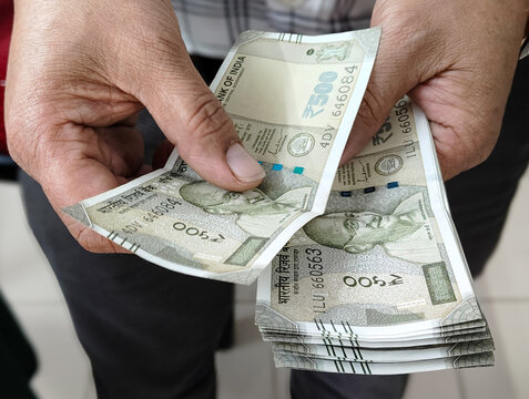 Hand holding five hundred indian currency note by unrecognizable man taking one note in right hand and rest in left hand