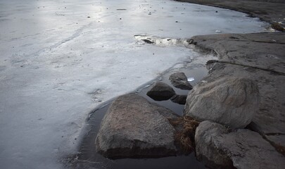 A large stone on the shore of a frozen lake in early spring
