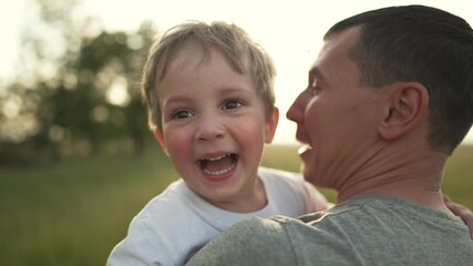 Father lifts son laughing in meadow father carries smiling son while parent and family enjoy outdoor summer hug and laugh in grassy meadow smiling child happy playful bond joyful smile hug together