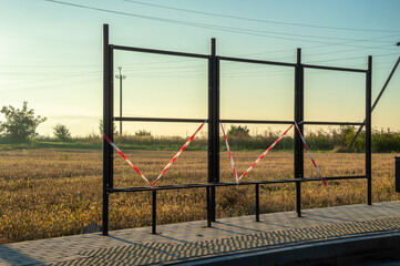 A bus stop frame stands empty and unoccupied in a wide field as the sun sets, marked with caution...