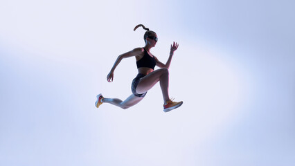 Fototapeta premium Futuristic athlete in dynamic mid-air leap against gradient light. Concept of high-performance training, agility drills, sports branding, and modern fitness visuals with energized motion.