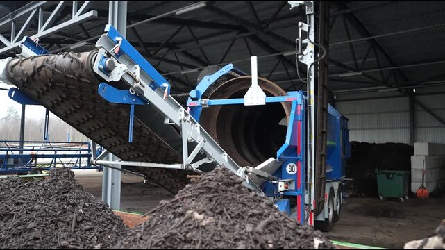Cesis, Latvia - November 21, 2025: Industrial machinery unloading compost material with conveyor system in action, camera pans and zooms for detail