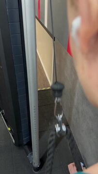 Young woman doing  triceps rope pushdowns on a cable machine at the gym, focused on strength training and building muscle for an active, healthy lifestyle while listening to music