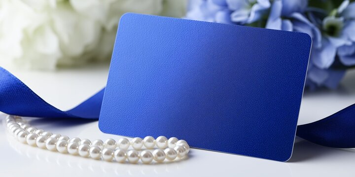 A close-up of a blank gift card mockup with a beautiful, deep sapphire blue color and a small, single-strand white pearl ribbon draped over it