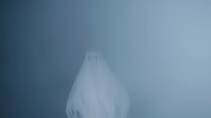 Figure draped in white sheet with eye holes; appears ghostly against a misty, bluish background - Powered by Adobe