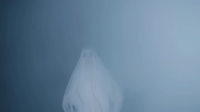 Figure draped in white sheet with eye holes; appears ghostly against a misty, bluish background