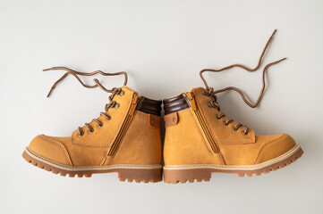 Stylish yellow and brown boots made of genuine leather nubuck on light gray background top view. Rough autumn-winter work boots with ribbed sole and laces. Men's, teenager, or children's footwear