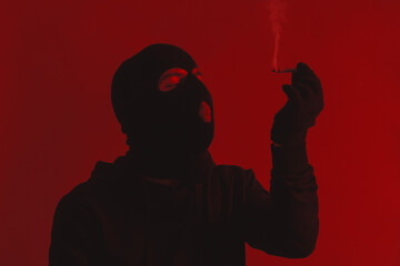 Man in Hoodie and Black Balaclava Closing Eyes While Holding a Lit Cigarette