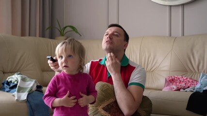 Parent and small child share absorbing home entertainment moment, intently watching screen together on sofa, highlighting their bond and mutual enjoyment.