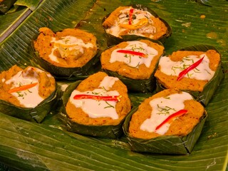 A neatly arranged display of Hor Mok pla chon, a traditional Thai steamed fish curry custard, shown in individual banana-leaf cups and set out for sale.