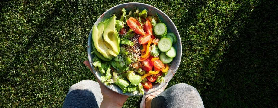 The salad bowl held over grass with avocado, tomatoes, cucumbers and greens - Powered by Adobe