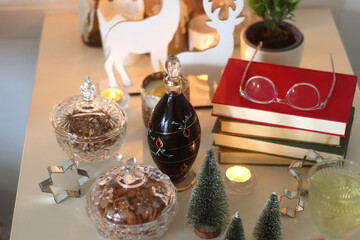 Cookie jar, tea, wine, nuts, books, lit candles and Christmas decorations on the table. Cozy Christmas hygge at home. Selective focus.