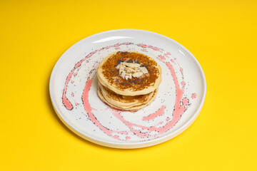 Stack of pancakes with syrup and nuts on yellow background