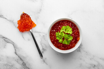 Top view of red caviar bowl with parsley and spoon on marble