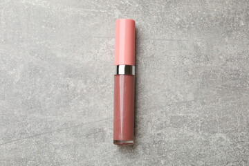 Beautiful pink lip gloss on grey textured background, top view