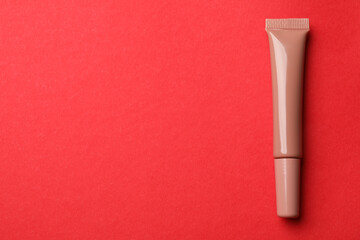 Beautiful nude lip gloss on red background, top view. Space for text