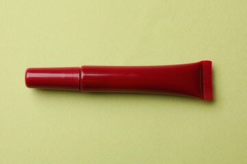 Beautiful dark red lip gloss on light green background, top view