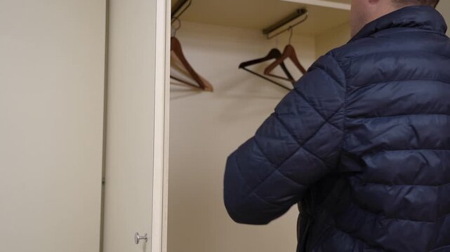 Man meticulously arranges garment in modern, neutral cabinet with sleek metallic hardware, showcasing organized storage.