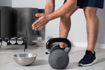 Man clapping hands with talcum powder before training with kettlebell in gym, closeup