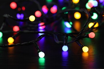 Bright Christmas lights glowing on table in darkness, closeup