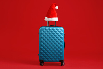 Christmas vacation. Blue suitcase with Santa hat on red background