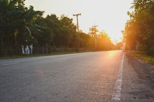 A country road at sunset with trees and power lines.