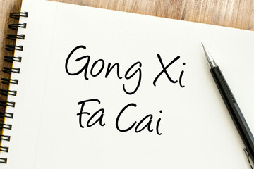 Handwritten Gong Xi Fa Cai phrase on a spiral notepad, conveying festive Lunar New Year wishes for prosperity and good fortune