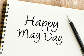 Happy May Day handwritten message on an open spiral notebook with a pen, celebrating the international labor and spring holiday