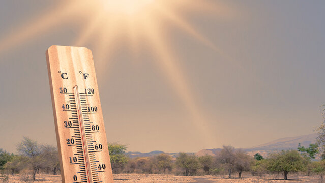Thermometer registering high temperatures with the sun drenched on an arid landscape background. Extreme weather background