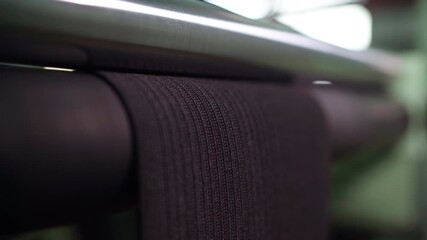 Black webbing moving over rollers, textured woven strap advancing under tension control, rubberized drums and steady progression, dim workshop lighting, implied quality inspection