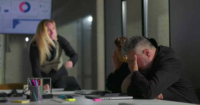 Female boss publicly scolding male employee during tense office meeting, man hides face in shame as colleagues look on, highlighting workplace conflict and humiliation