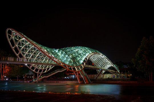 Illuminated Peace Bridge spanning Kura River in Tbilisi at night