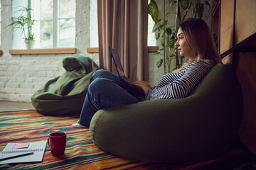 Woman working on laptop in cozy home interior with warm daylight. Concept of business lifestyle,...