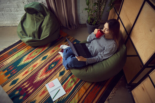 Woman drinking coffee while working on laptop in relaxed home setting. Concept of lifestyle productivity, morning rituals, beverage marketing, remote-work storytelling, and creativity visuals.